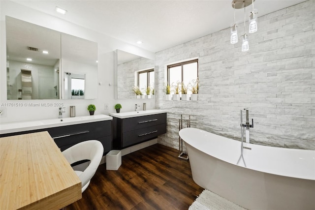 full bathroom with a sink, a freestanding tub, two vanities, and wood finished floors