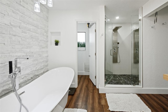 full bath featuring a shower stall, a freestanding tub, wood finished floors, and baseboards