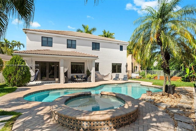 rear view of house with a pool with connected hot tub, fence, a tile roof, stucco siding, and a patio area