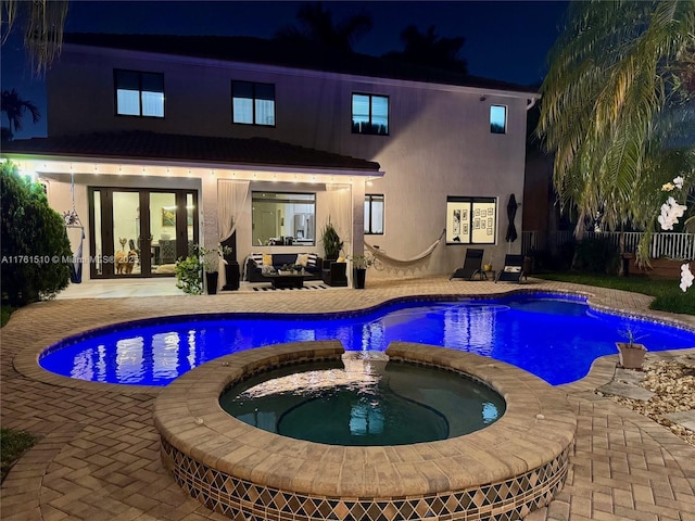 pool at night featuring a patio, french doors, a pool with connected hot tub, and an outdoor hangout area