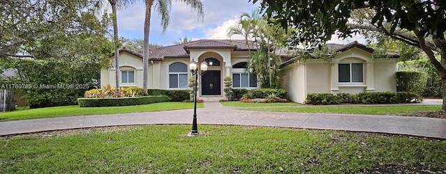 mediterranean / spanish home with a front lawn, a tiled roof, driveway, and stucco siding