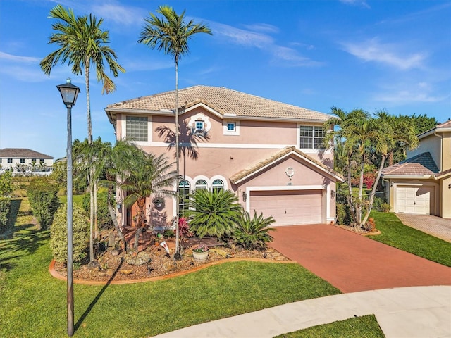 mediterranean / spanish-style home with stucco siding, a garage, a front lawn, and a tile roof