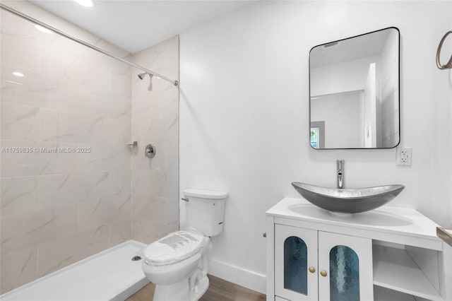 bathroom featuring a tile shower, toilet, vanity, and baseboards