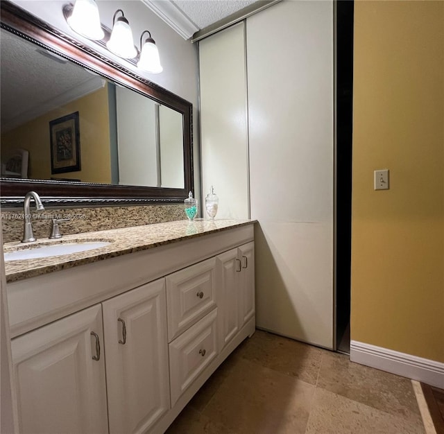 bathroom with baseboards, a textured ceiling, ornamental molding, and vanity