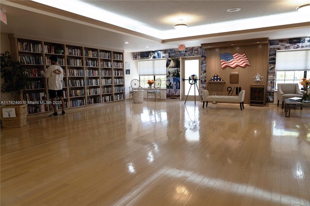 miscellaneous room featuring wall of books, a textured ceiling, a tray ceiling, and hardwood / wood-style flooring