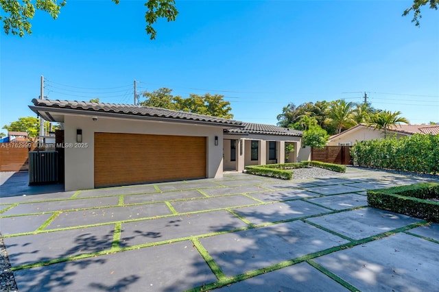 view of front of home with stucco siding, driveway, a tile roof, fence, and an attached garage