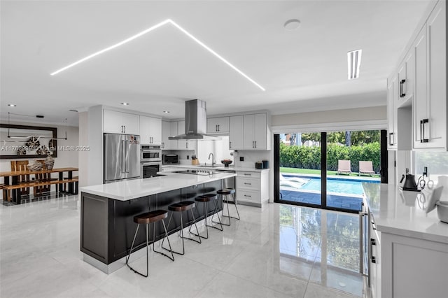 kitchen featuring a breakfast bar area, light countertops, appliances with stainless steel finishes, island exhaust hood, and a sink