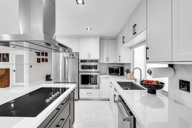 kitchen featuring light stone counters, appliances with stainless steel finishes, island range hood, white cabinets, and a sink