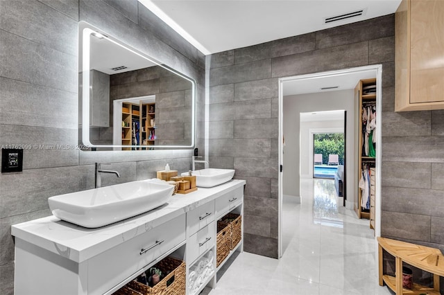 bathroom with visible vents, double vanity, a sink, a walk in closet, and tile walls