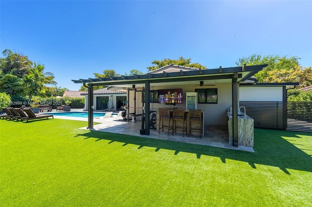 rear view of house featuring fence, stucco siding, a patio area, a lawn, and outdoor dry bar