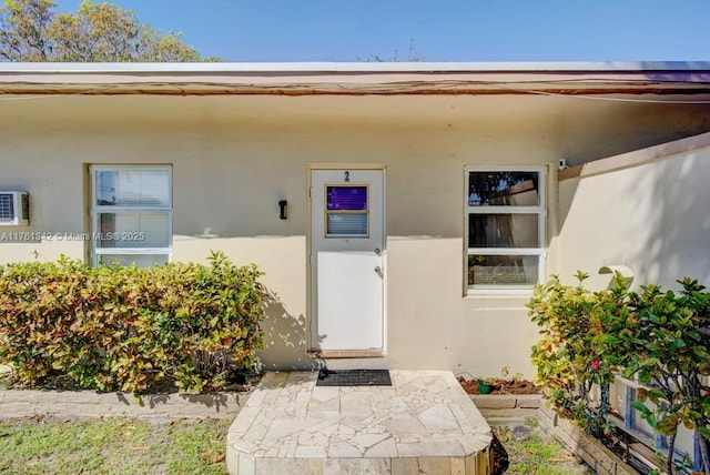 view of exterior entry featuring stucco siding and a wall mounted AC