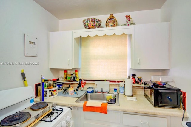 kitchen featuring a sink, white gas stove, white cabinets, and light countertops