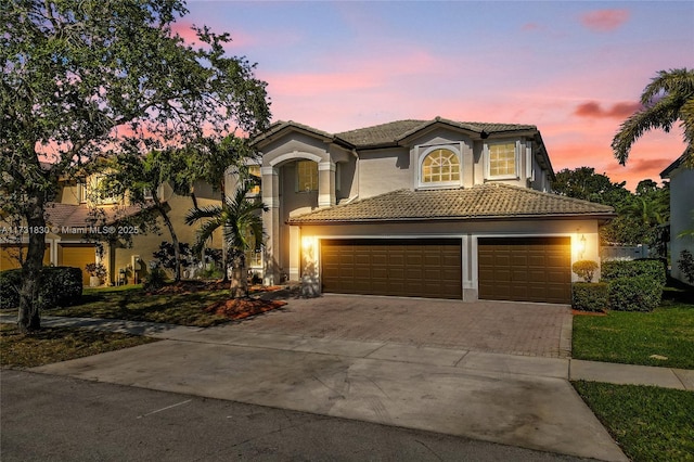 mediterranean / spanish house with a tiled roof, an attached garage, driveway, and stucco siding