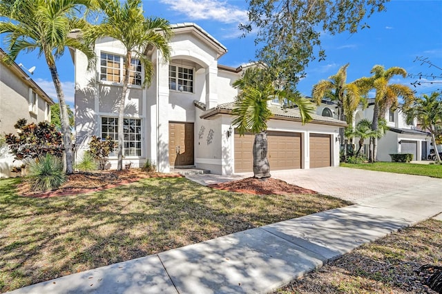 mediterranean / spanish house featuring stucco siding, a front lawn, a garage, and driveway