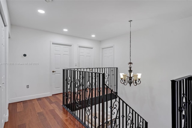 hall featuring baseboards, an upstairs landing, recessed lighting, wood finished floors, and a notable chandelier