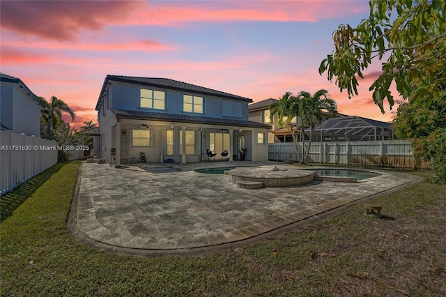 back of house at dusk with a patio area, a yard, a fenced backyard, and a fenced in pool