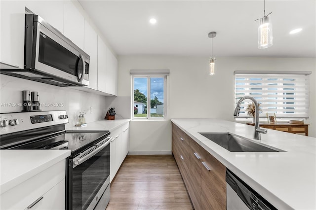 kitchen featuring light wood-style flooring, a sink, stainless steel appliances, white cabinets, and modern cabinets