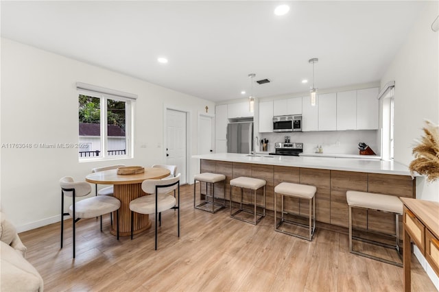 kitchen with stainless steel appliances, light countertops, white cabinetry, a kitchen breakfast bar, and light wood-type flooring