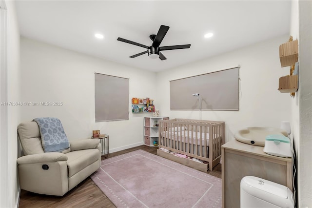 bedroom with wood finished floors, baseboards, a ceiling fan, recessed lighting, and a crib