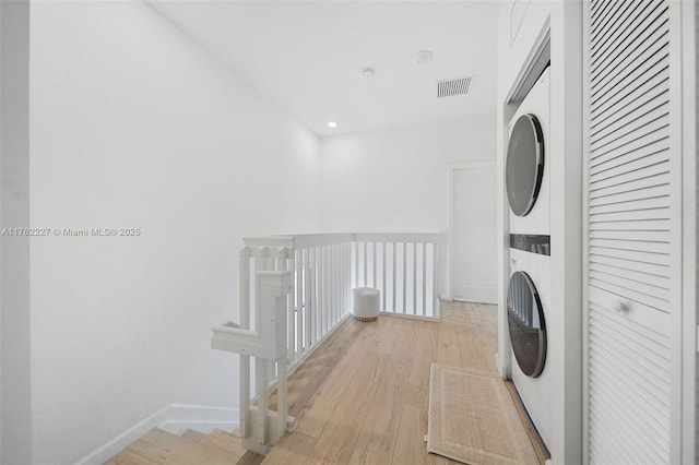 laundry area with laundry area, light wood-style floors, visible vents, and stacked washing maching and dryer