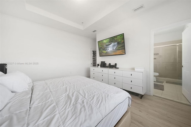 bedroom with light wood finished floors, visible vents, connected bathroom, and a raised ceiling