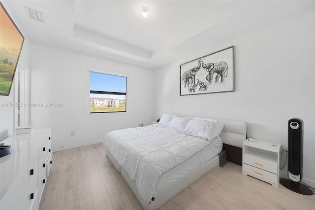 bedroom with a tray ceiling, baseboards, visible vents, and light wood finished floors