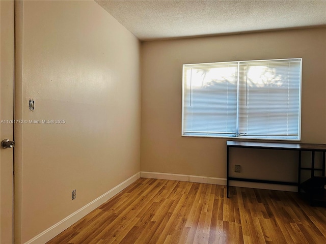 spare room with baseboards, a textured ceiling, and wood finished floors