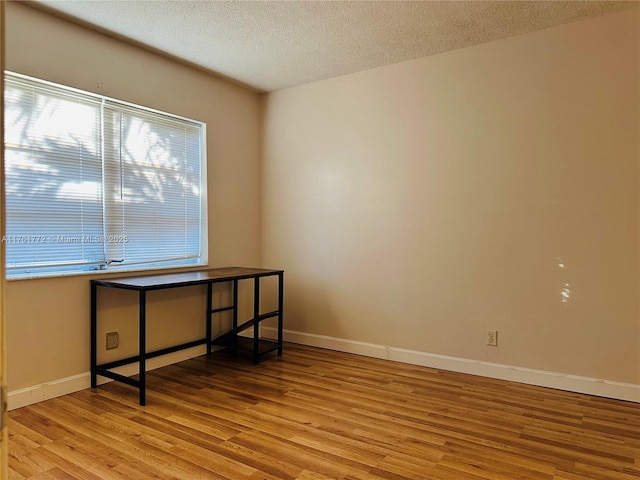 empty room with baseboards, light wood finished floors, and a textured ceiling