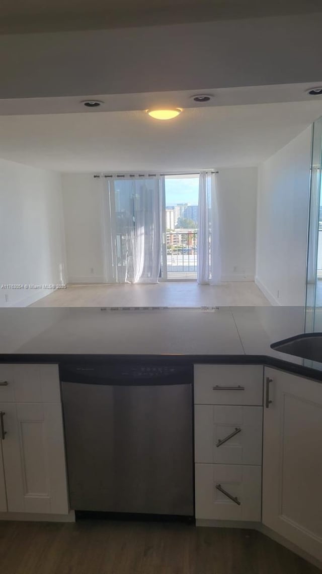 kitchen with stainless steel dishwasher, dark countertops, wood finished floors, and white cabinetry