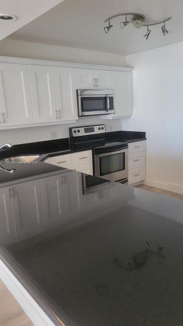 kitchen featuring a sink, dark countertops, wood finished floors, stainless steel appliances, and white cabinets