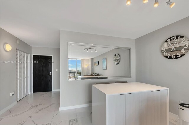 interior space featuring track lighting, baseboards, marble finish floor, and light countertops