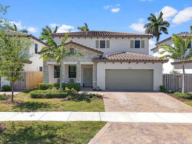 mediterranean / spanish-style house with decorative driveway, fence, stone siding, and an attached garage