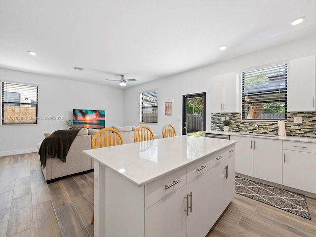 kitchen with light wood-type flooring, a sink, a kitchen island, tasteful backsplash, and white cabinetry