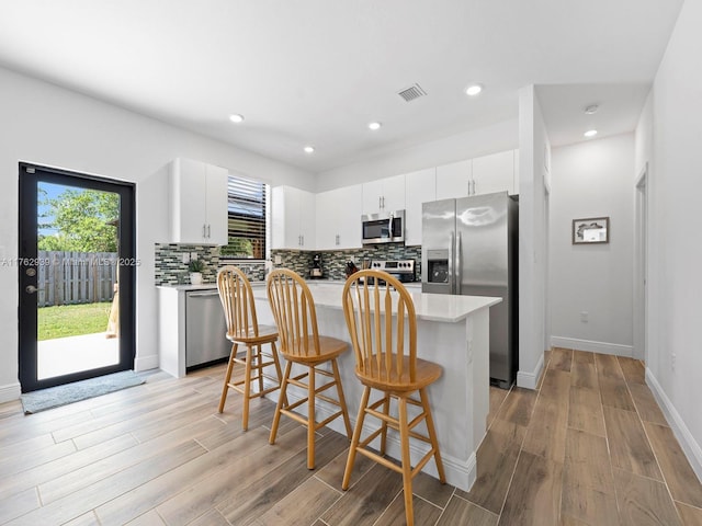 kitchen featuring visible vents, backsplash, a kitchen island, appliances with stainless steel finishes, and a breakfast bar area