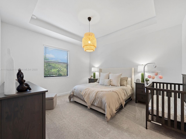 bedroom with a raised ceiling, baseboards, and light carpet