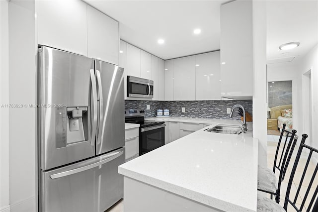 kitchen featuring modern cabinets, a sink, backsplash, white cabinetry, and appliances with stainless steel finishes