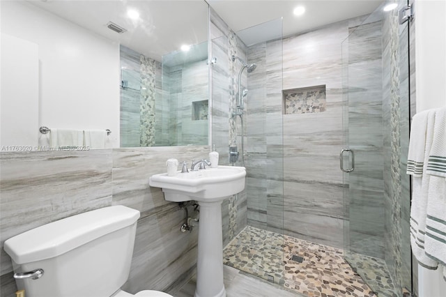 bathroom featuring tile walls, toilet, visible vents, and a stall shower