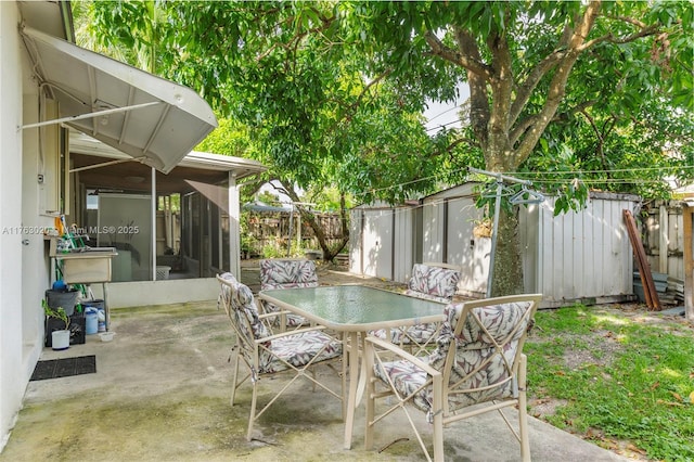 view of patio with a shed, a fenced backyard, a sunroom, an outbuilding, and outdoor dining space