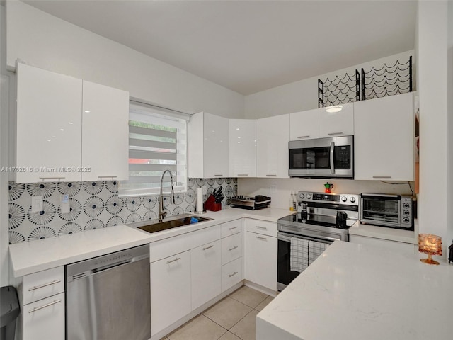 kitchen featuring a sink, stainless steel appliances, a toaster, white cabinets, and light countertops