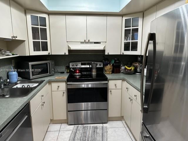 kitchen featuring under cabinet range hood, a sink, appliances with stainless steel finishes, light tile patterned flooring, and white cabinets