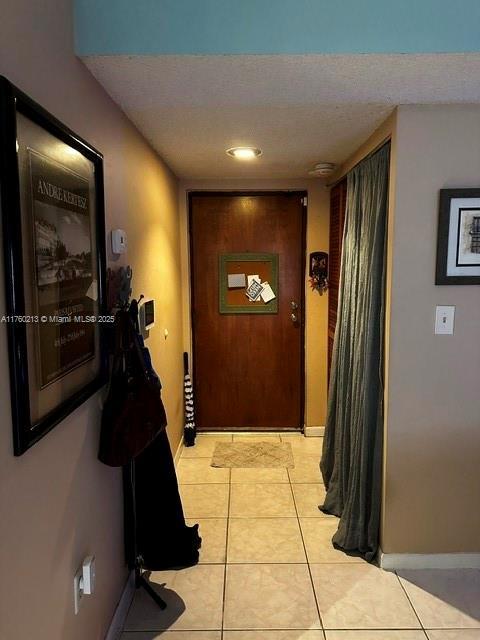 hall with light tile patterned flooring, a textured ceiling, and baseboards