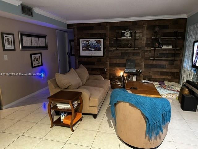 tiled living area featuring visible vents, baseboards, and ornamental molding