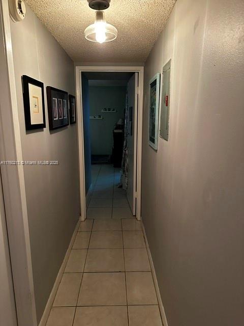 hallway with light tile patterned floors, baseboards, and a textured ceiling