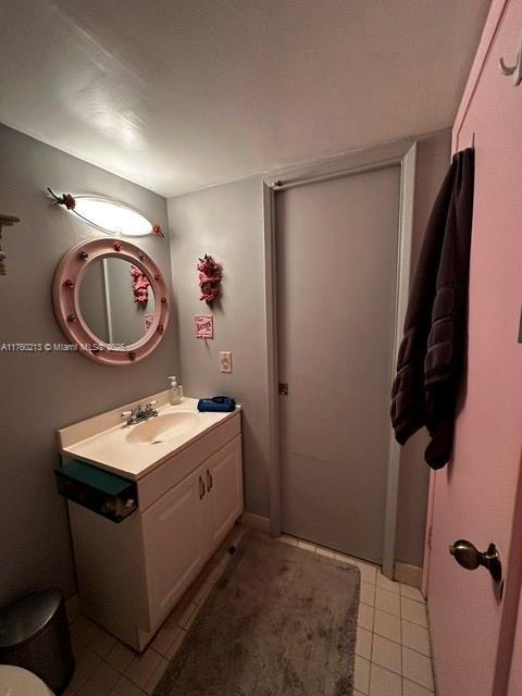 half bath featuring baseboards, toilet, vanity, and tile patterned flooring