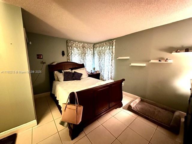 bedroom with light tile patterned floors, a textured ceiling, and baseboards