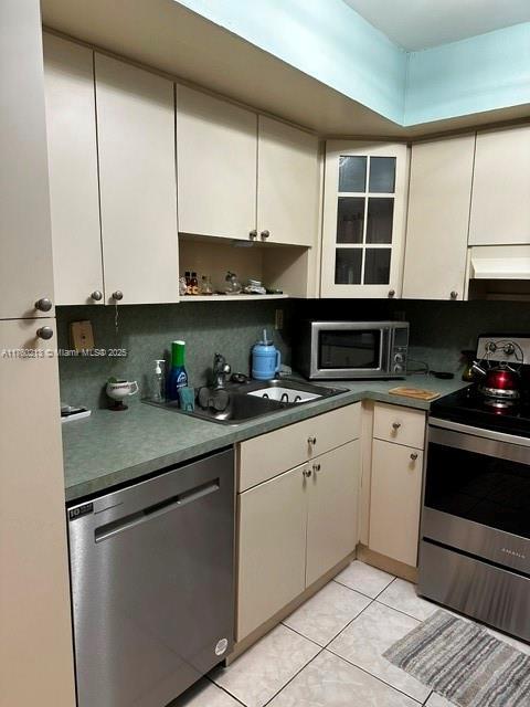 kitchen with light tile patterned floors, a sink, under cabinet range hood, appliances with stainless steel finishes, and tasteful backsplash