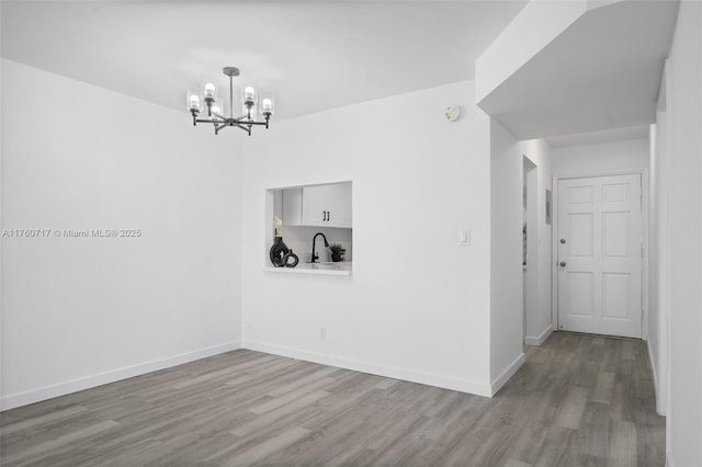 unfurnished room with a sink, a chandelier, baseboards, and wood finished floors