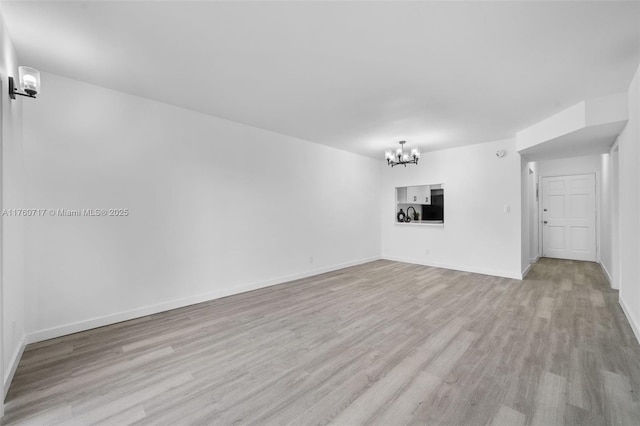 unfurnished living room featuring light wood-type flooring, baseboards, and an inviting chandelier