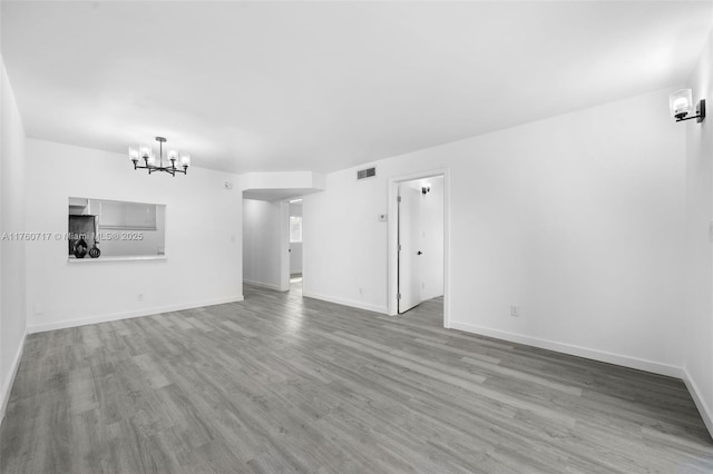 unfurnished living room featuring visible vents, an inviting chandelier, baseboards, and wood finished floors