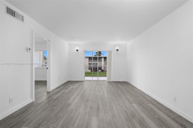 empty room featuring visible vents, plenty of natural light, baseboards, and wood finished floors